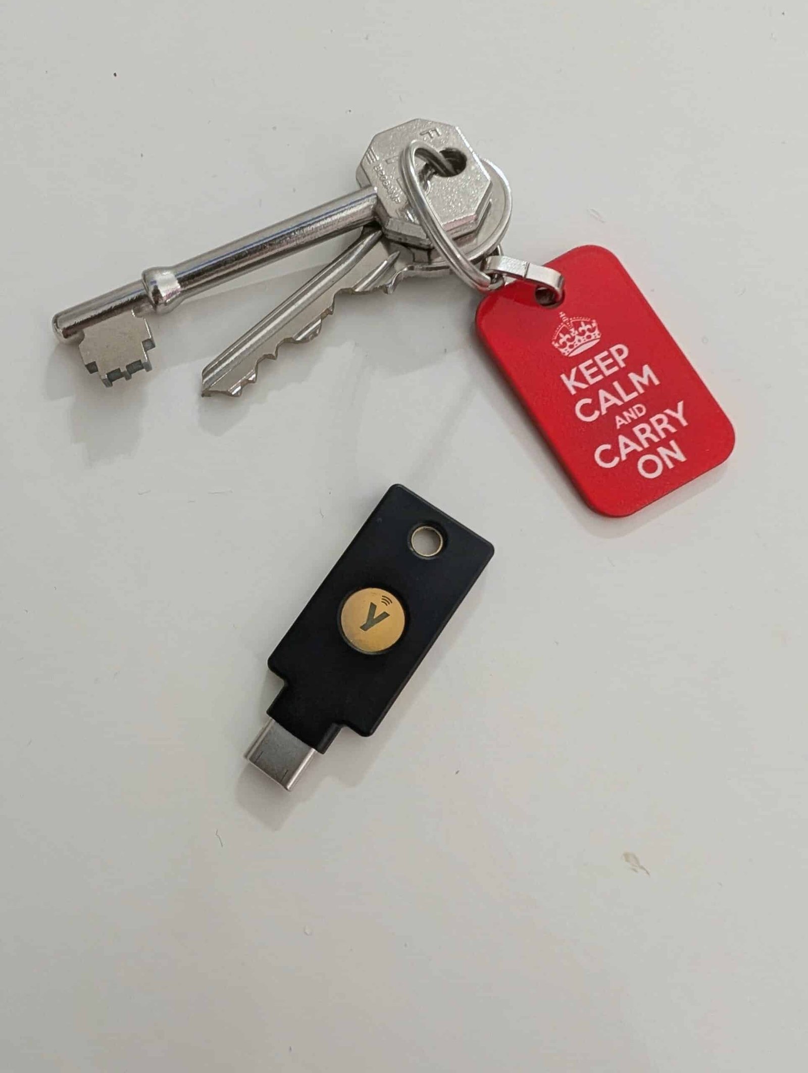 A YubiKey 5C sitting next to a set of house keys with a Keep Calm and Carry On keyring
