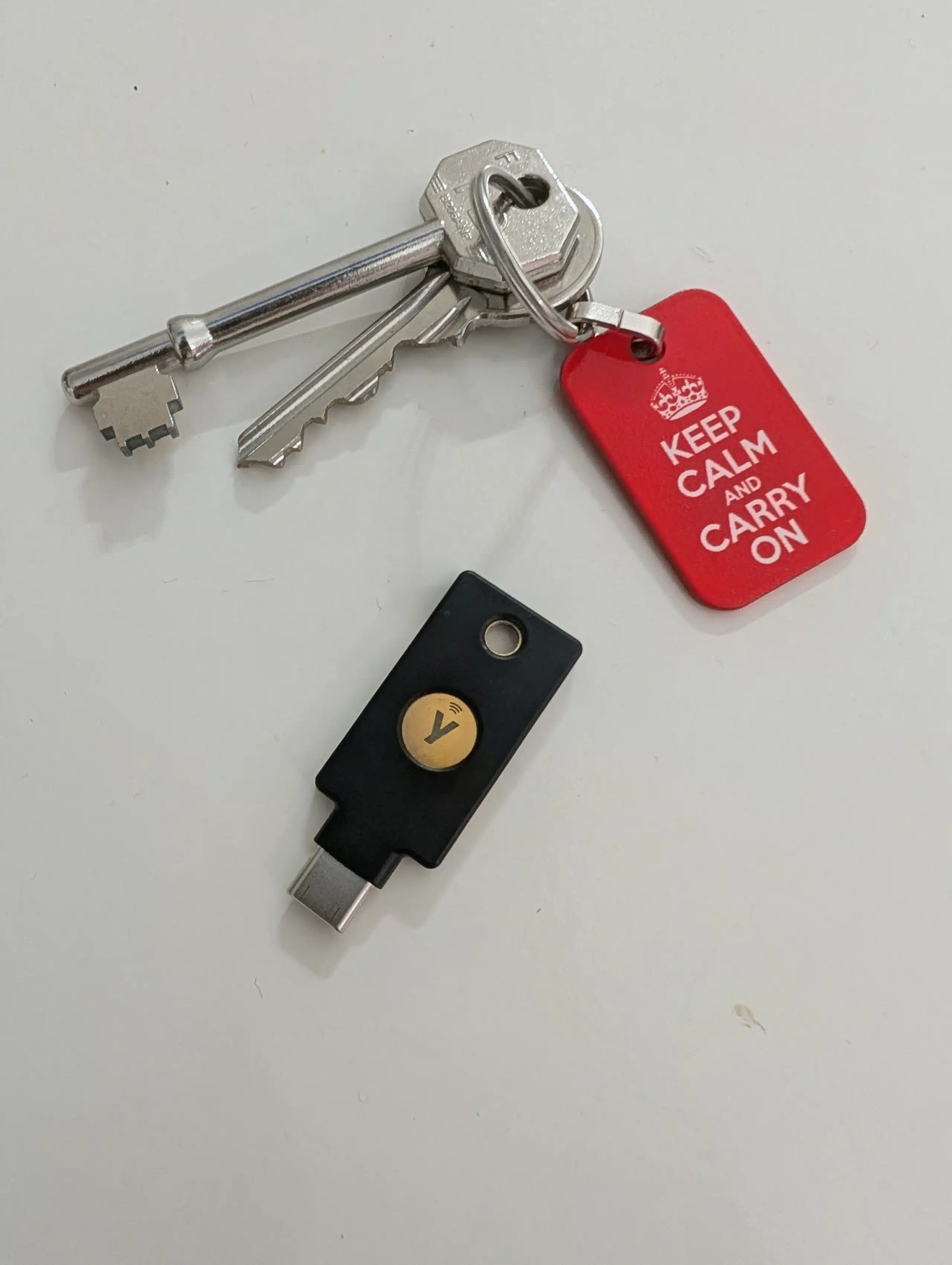 A YubiKey 5C sitting next to a set of house keys with a Keep Calm and Carry On keyring